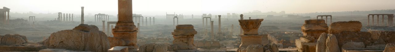 Panoramabild von Palmyra. Antike Ruinen - Säulen und Arkaden - säumen eine trockene, dunstige Landschaft.